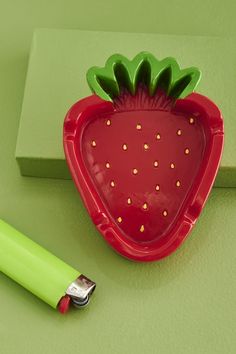 a red strawberry shaped plate next to a green pen and eraser on a green surface