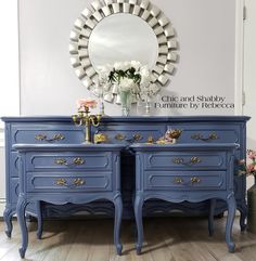 a blue dresser with flowers on top and a mirror above it