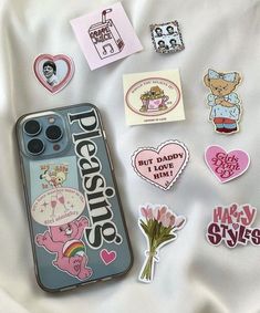 various stickers and magnets are laying on a bed sheet with a phone case