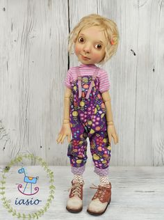 a doll with blonde hair wearing overalls and pink shirt standing in front of a wooden wall