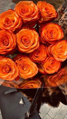 a bouquet of orange roses sitting on top of a table next to a handbag