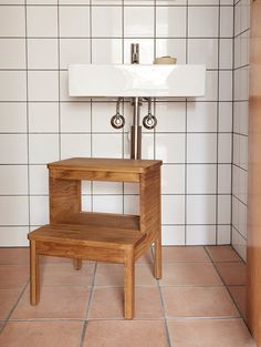 a small wooden step stool sitting in front of a white sink and tiled bathroom wall