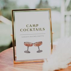 a sign that says camp cocktails on it next to a feathery white object