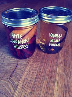 two jars filled with apple cinnamon whiskey sitting on top of a wooden table next to each other