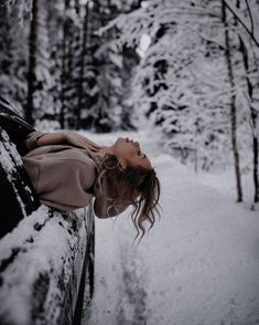 a woman laying on top of a car in the snow next to trees and bushes