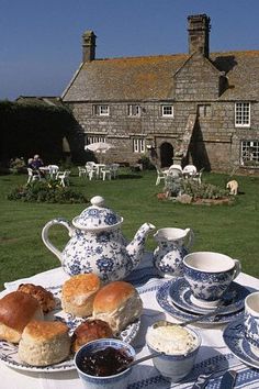 the table is set with bread, butter and jams on it in front of an old stone house