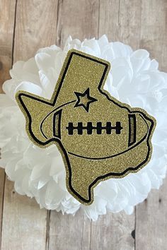 a gold glitter texas shaped football ornament sitting on top of a white ruffled pillow