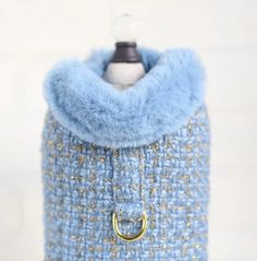 a blue and gold tweed bag with a metal ring on the front, hanging from a hook