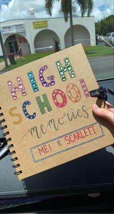 a hand holding up a notebook with the words high school memories written on it in front of a car