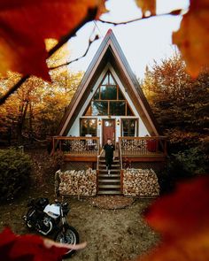 a man standing in front of a house with a motorcycle parked next to it and autumn leaves on the ground