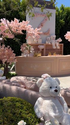 a white teddy bear sitting on top of a lush green field next to pink flowers