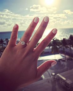 a woman's hand with a diamond ring on it, overlooking the ocean and palm trees