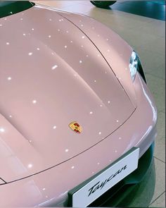 a pink sports car parked in a showroom with its hood up and the emblem on it