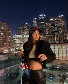 a woman standing on top of a roof in front of a cityscape at night