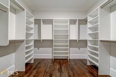 an empty walk - in closet with white shelving and wooden flooring is shown