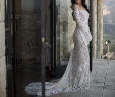 a woman standing in front of a glass door wearing a wedding dress with long sleeves