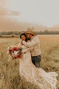 a bride and groom hugging in the middle of a field at sunset with an orange sky behind them