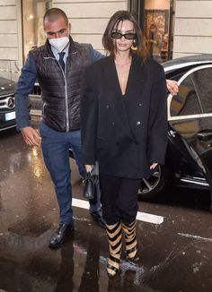 a woman in black jacket and striped tights walking next to a man wearing a face mask