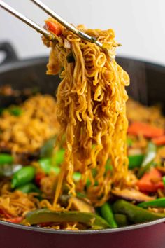 noodles being cooked in a pan with chopsticks over them and vegetables on the side