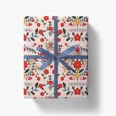 a gift wrapped in white paper with blue ribbon and floral designs on it, sitting against a white background