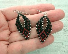 a pair of black, red and white beaded earrings on a person's hand