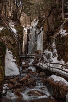 a small waterfall in the middle of a forest with snow on the ground and steps leading up to it