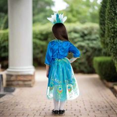 Spread those elegant wings and fly door to door on Halloween wearing this Peacock Costume. Colorful dress and wings display vibrant colors of indigo, aquamarine, and emerald, with hints of gold embroidery at the front and the hem of the dress. Feathery headpiece also included to top off your look. Product comes complete with: Dress and Headpiece Blue Satin dress has a Velcro closure in the back Peacock feathers can be open or closed, elastic loops for the wrists are on the feathers to keep in pl Peacock Fancy Dress For Kids, Peacock Carnival Costume, Peacock Costumes Women's, Girls Peacock Costume, Peacock Doll Dress, Peacock Costume, Blue Satin Dress, Celebration Balloons, Sticky Note Planner