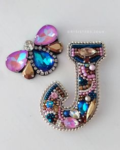 two colorful brooches sitting next to each other on a white surface and one has a letter made out of beads