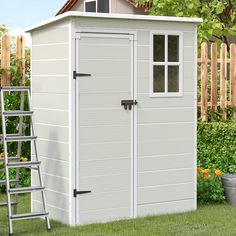 a white storage shed sitting in the grass next to a ladder and flower potted plant