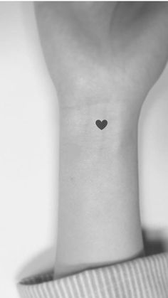 a small heart tattoo on the back of a woman's left arm, in black and white