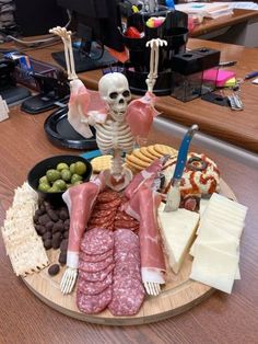 a wooden plate topped with meats and cheeses next to a skeleton on a table