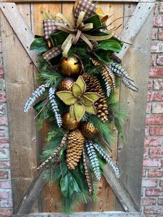 a christmas wreath with pine cones and evergreens on a wooden door hanger in front of a brick wall