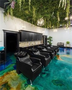 a room with several black chairs and plants hanging from the ceiling above them, in front of a bar