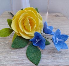 a yellow rose and two blue flowers sitting on top of a wooden table next to each other