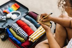 a woman sitting on the floor next to an open suitcase filled with clothes and other items