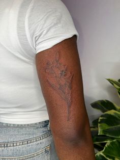 a man with a tattoo on his arm and shoulder is standing next to a potted plant