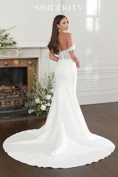 a woman in a white wedding dress standing next to a fireplace with flowers on it