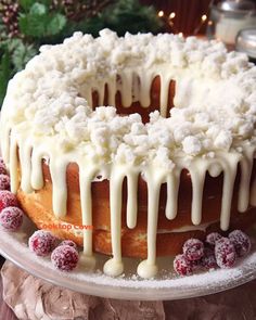 a cake with white icing and cranberries on a platter next to a christmas tree