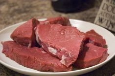 some meat is on a white plate next to a wine bottle and a glass in the background