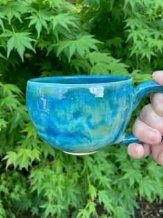 a hand holding a blue coffee cup in front of green plants