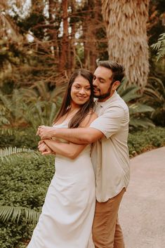 a man and woman hugging each other in the middle of a path surrounded by palm trees