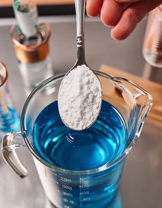 a spoon filled with blue liquid and powdered sugar on top of a measuring cup