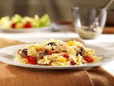 a white plate topped with pasta covered in meat and veggies next to a bowl of salad