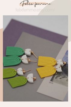 three pairs of colorful earrings on top of a table next to a card and envelope