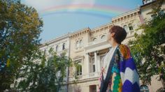 a woman standing in front of a building under a rainbow