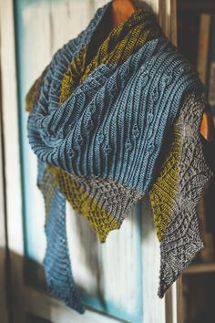 a blue and yellow knitted shawl hanging from a hook on a wooden door