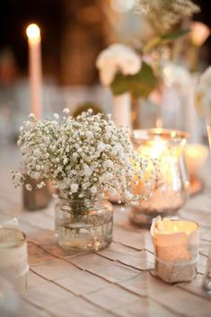 a table topped with vases filled with baby's breath next to lit candles