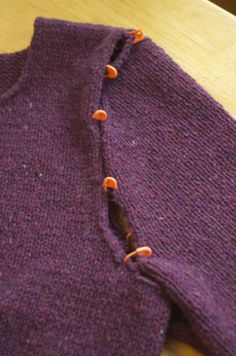 a close up of a purple sweater with orange buttons on the front and back, sitting on a wooden table