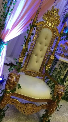 a fancy chair with gold trimmings and white upholstered seat is surrounded by greenery