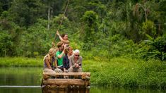 a group of people riding on the back of a wooden boat in a river surrounded by greenery